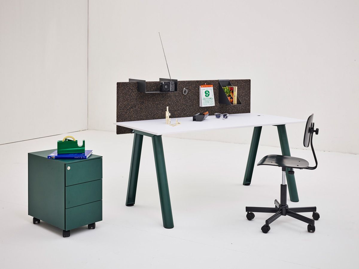 Interno di una stanza bianca con una cassettiera verde e una scrivania con attrezzi di lavoro